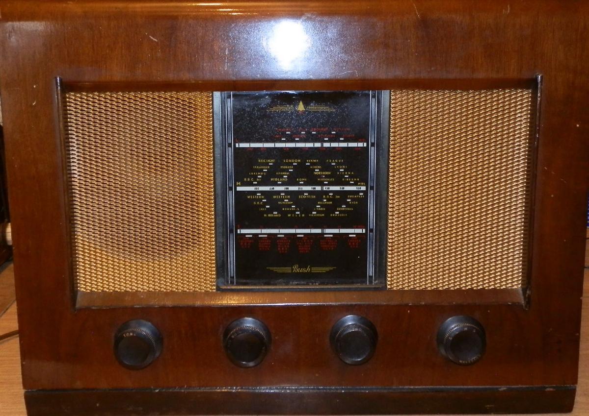 Walnut cabinet with speaker cloth on either side of a central black tuning scale and four brown knobs along the bottom
