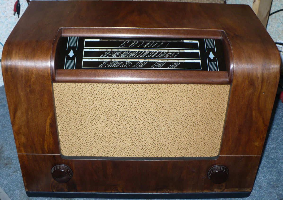 Rounded walnut cabinet with a horizontal tuning scale across the top, a gold speaker cloth below it and a knob at each lower corner