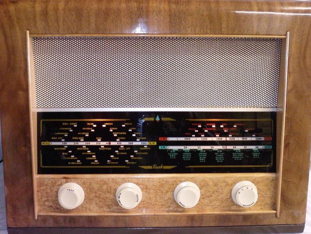 Walnut cabinet with a silver mesh speaker grille above a wide black tuning scale and four cream knobs on a pale wood strip