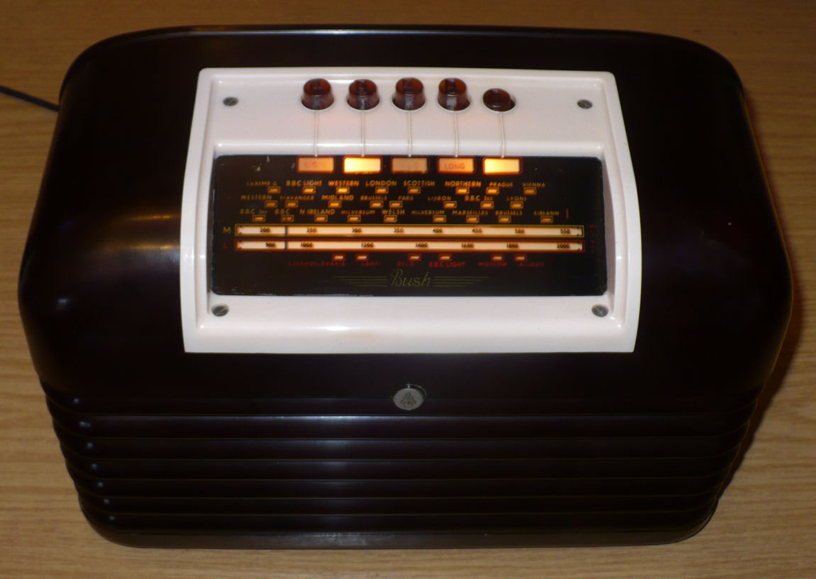 Black Bakelite radio with a ribbed lower front and a cream control panel carrying five brown knobs above a lit tuning scale