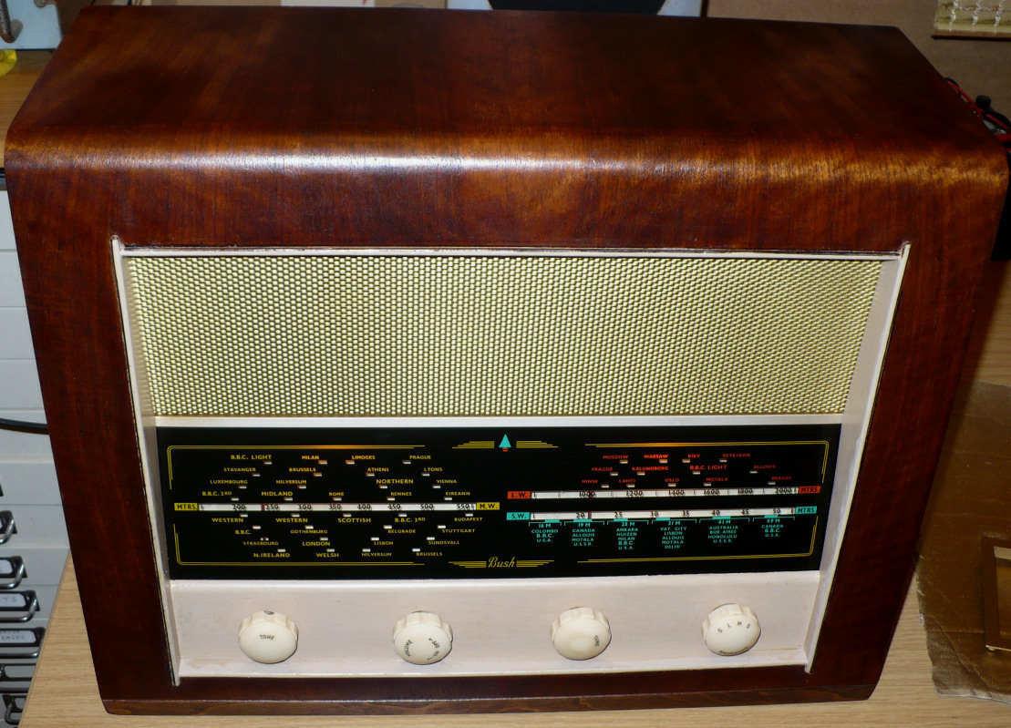 Walnut cabinet with a gold speaker grille above a black tuning scale and four cream knobs along the bottom