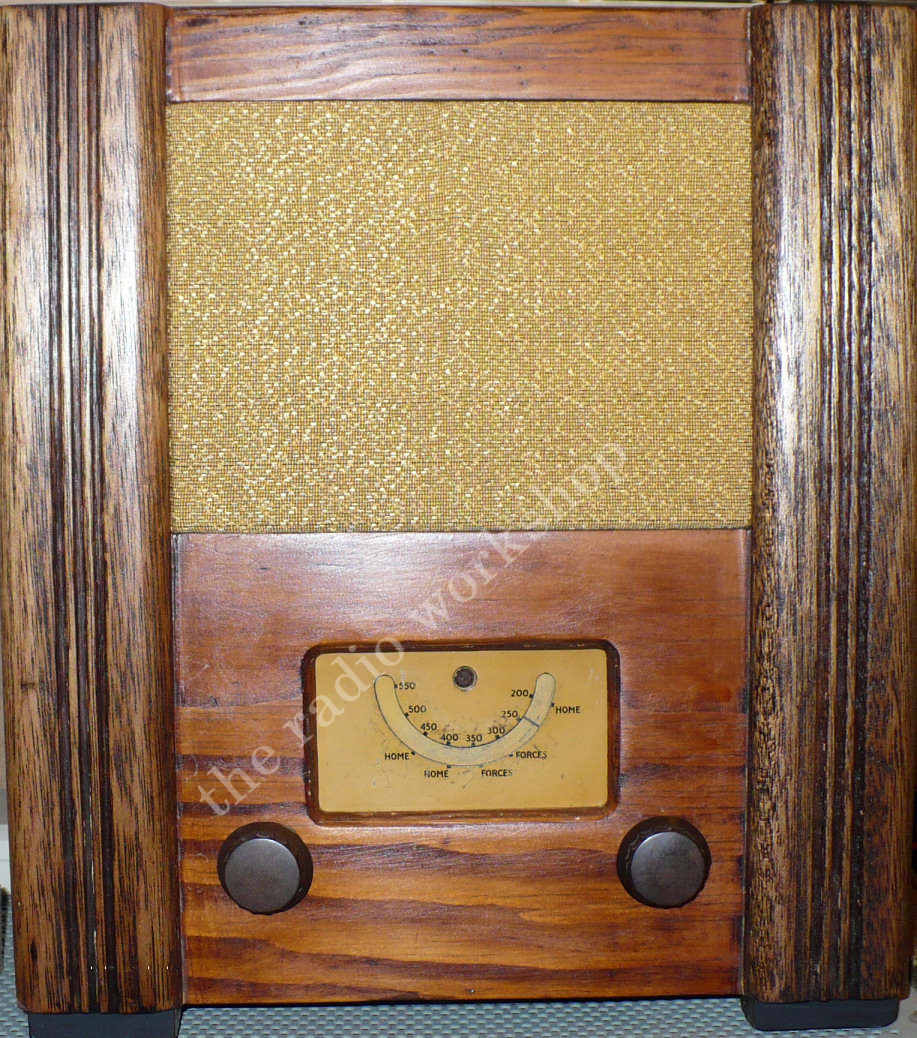 Tall oak-framed cabinet with a gold speaker cloth above a small curved tuning dial and two brown knobs