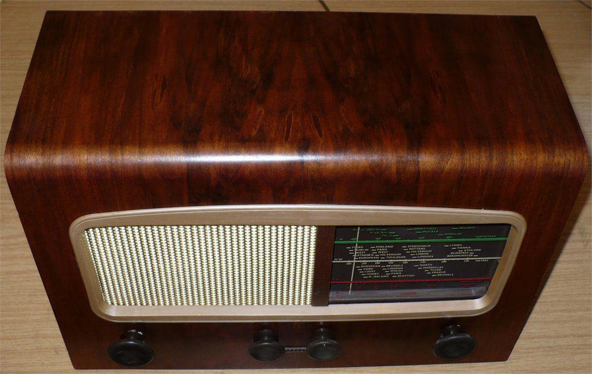 Walnut cabinet with a cream metal speaker grille and a small tuning scale on the right, above a row of four knobs