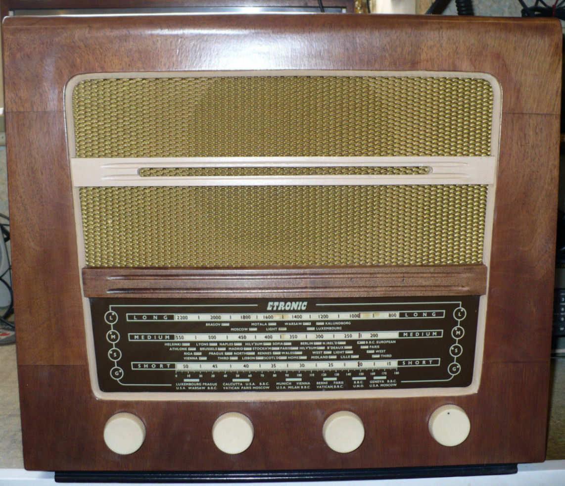 Walnut cabinet with a gold speaker cloth above a wide tuning scale and four cream knobs