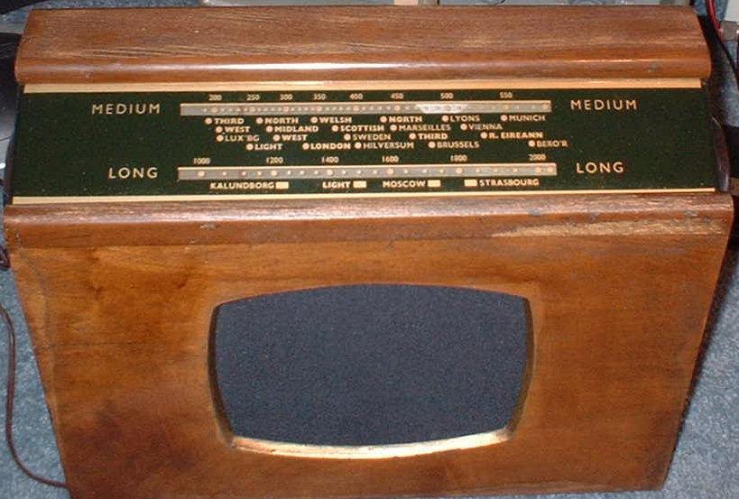 Light wood cabinet with a green tuning scale across the top and a rectangular grey speaker opening on the front