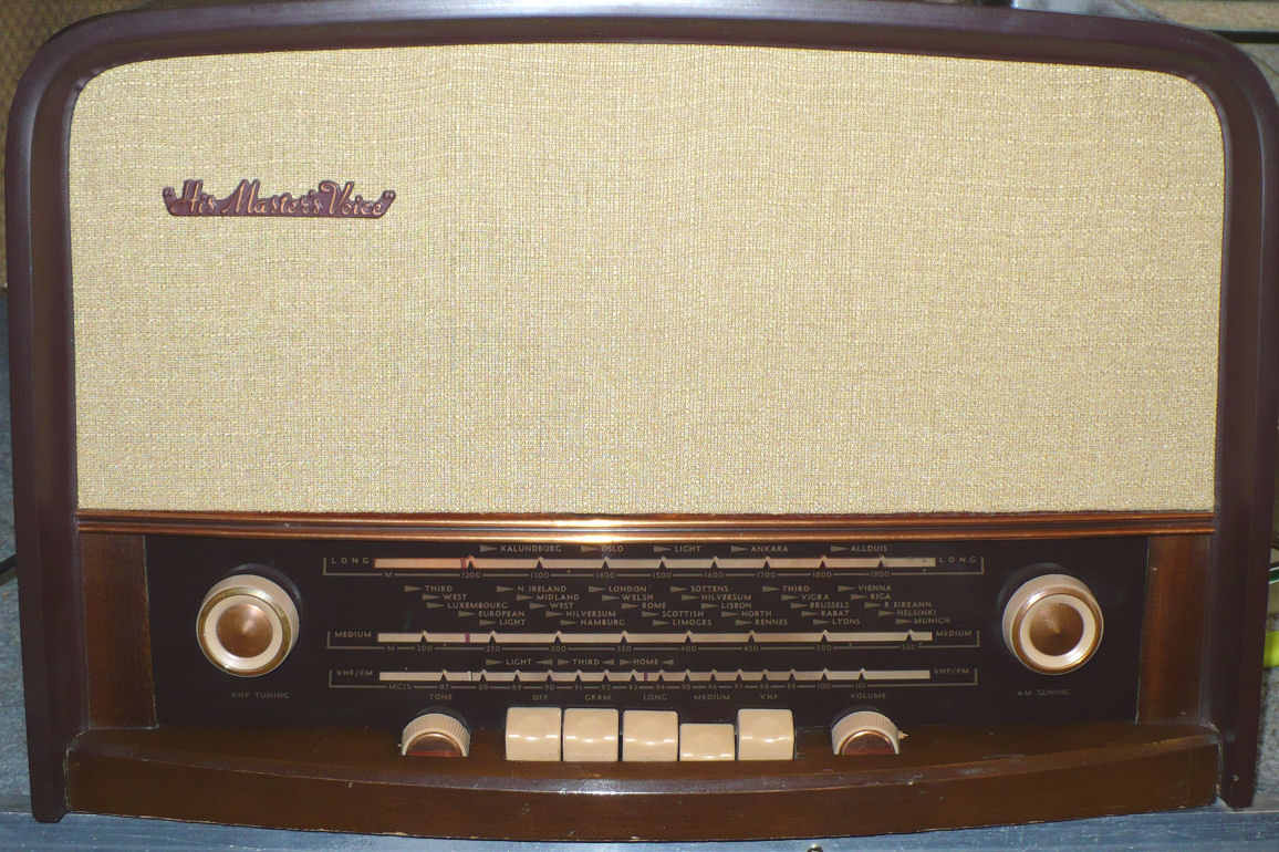 Dark wood cabinet with a cream speaker cloth above a tuning scale, two cream knobs and a row of push buttons