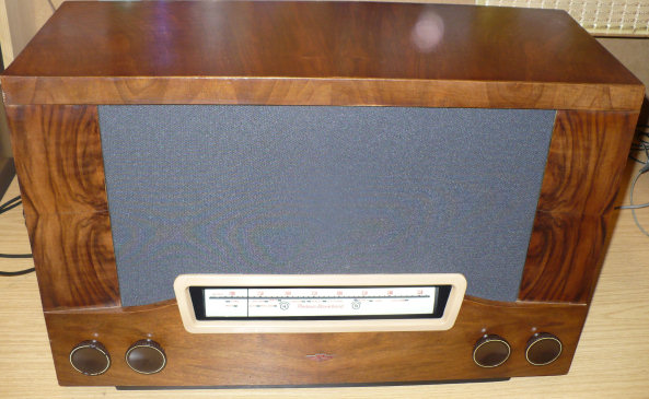 Walnut cabinet with a grey speaker cloth above a small tuning scale in a cream surround, and a pair of knobs at each lower corner