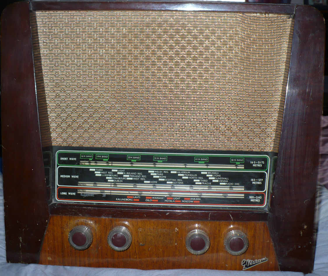 Dark wood cabinet with a woven speaker cloth above a green tuning scale and four brown knobs