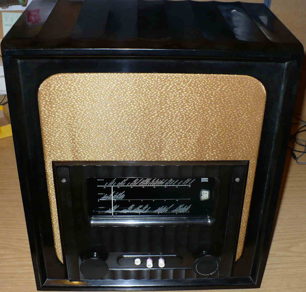 Black Bakelite cabinet with a gold speaker cloth above a dark tuning scale window and three small switches