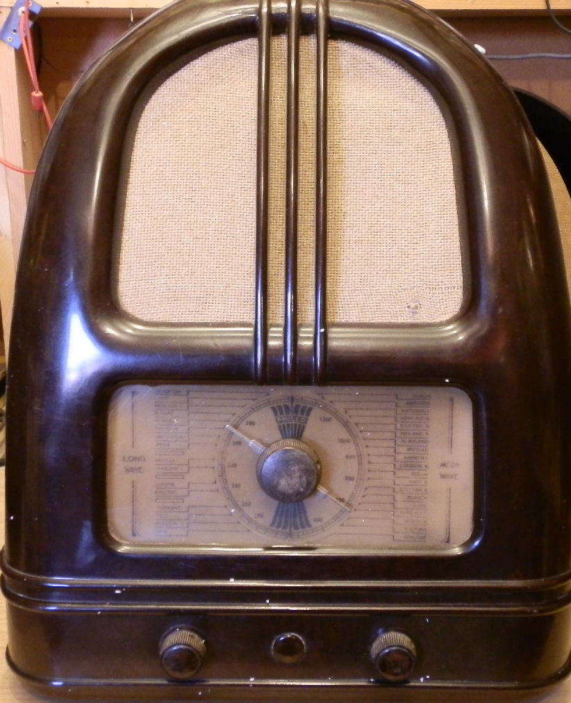 Dark brown Bakelite radio shaped like an arch with vertical ribs, a speaker cloth above a round dial and three knobs