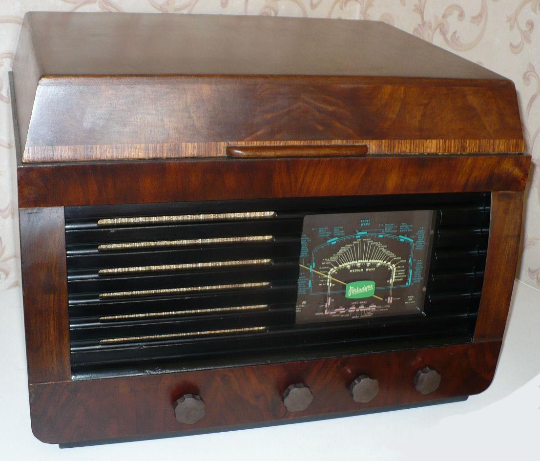 Walnut cabinet with a hinged lid, horizontal speaker bars on the left, a green tuning dial on the right and four knobs below