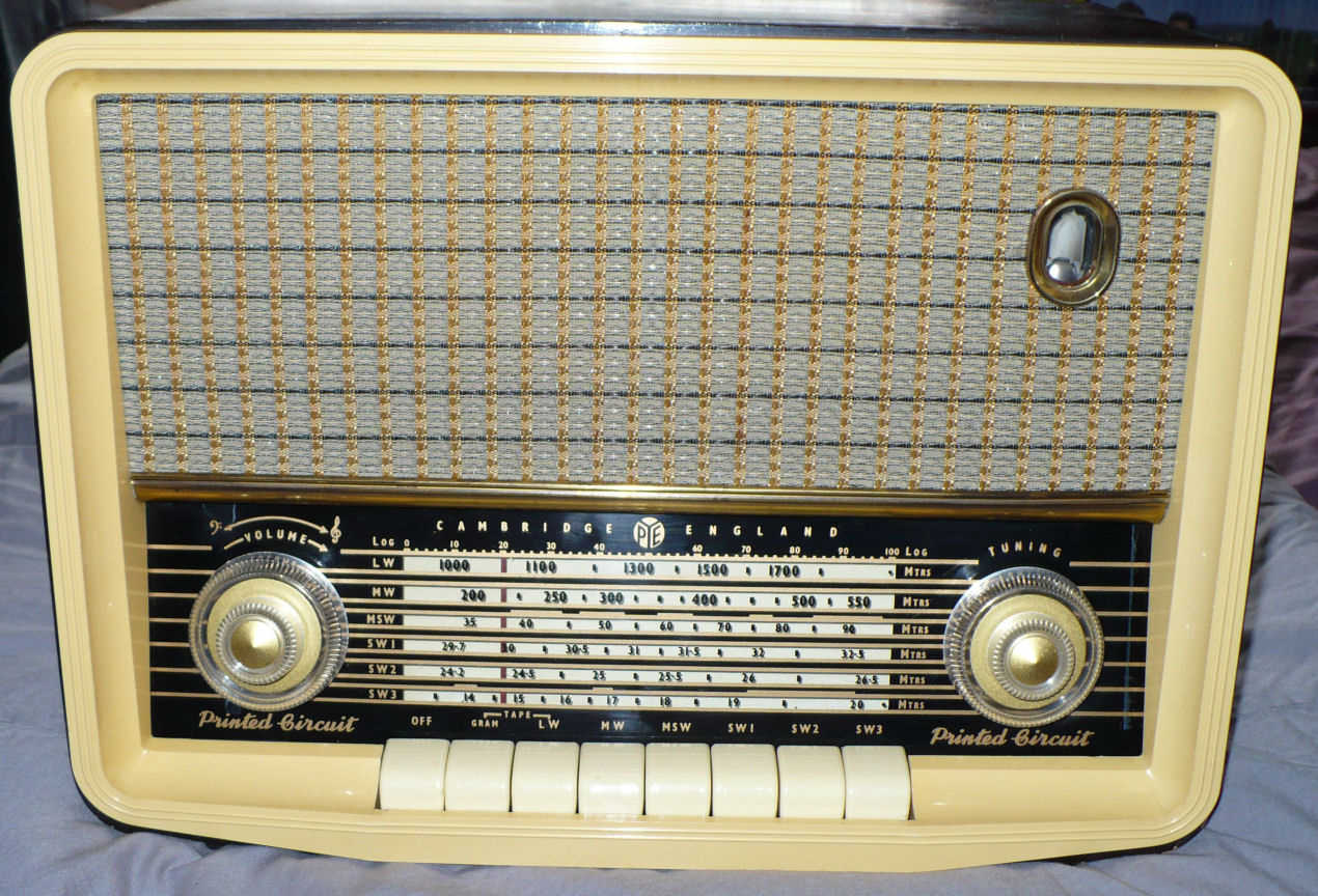 Cream radio with a speaker grille in the upper half, a wide black tuning scale with two large knobs and a row of cream push buttons below