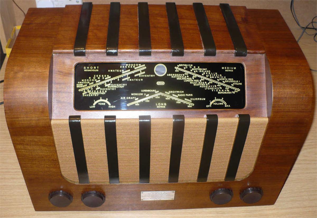 Walnut cabinet with black vertical bars across the top and front, a black tuning scale with crossed wavelength lines and four brown knobs