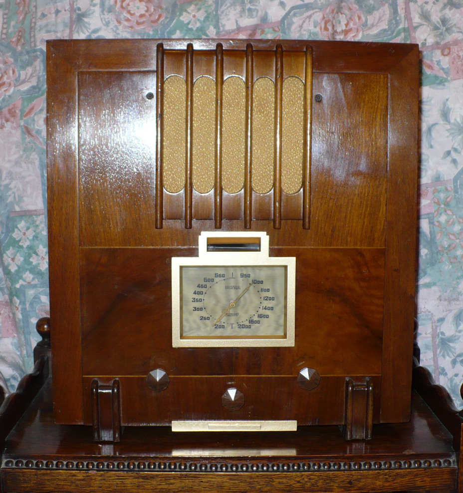 Walnut cabinet with vertical speaker slots at the top, a cream-framed tuning dial below and three controls along the bottom